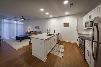 A kitchen with white cabinets, stainless steel appliances, wood-look flooring which opens into living room at Wesley Place Apartments in Indianapolis, IN